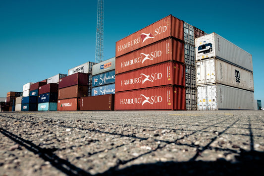 Stacked shipping containers at a commercial port under clear blue sky, featuring brands like Hamburg Süd, MSC, Maersk, and Hyundai – global logistics and international freight transport concept